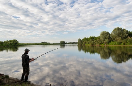 Fishing in river a fisherman with a fishing rod on the river bank. man fisherman catches a fish